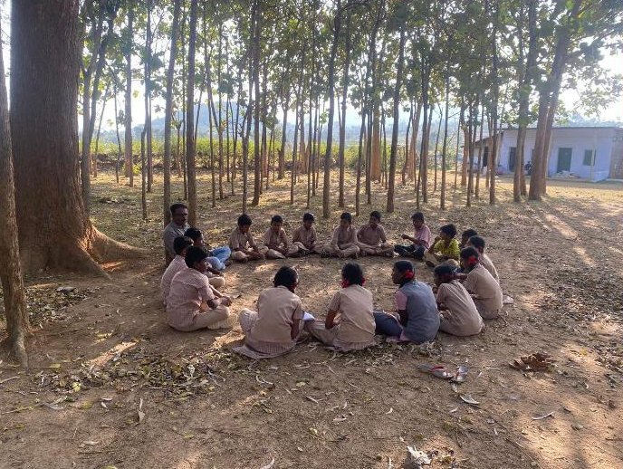 Children sitting in a circle for a community workshop in a forest clearing