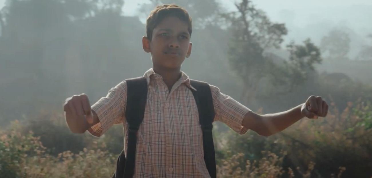 A schoolboy with a backpack stands with arms spread in morning mist