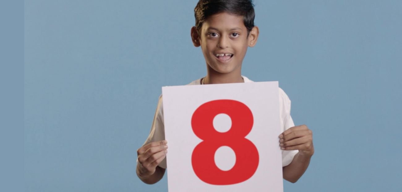A smiling boy holding a card with a large red number 8